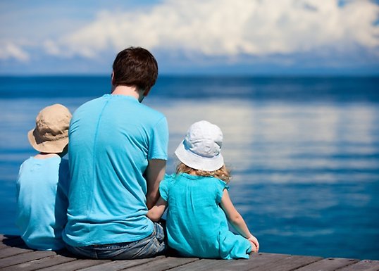 Father sitting on a dock with two children looking at the horizon.