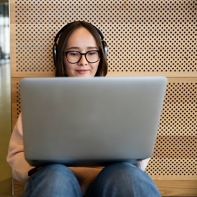 Kvinna sitter på golvet med laptop och hörlurar, lutar sig mot en akustikvägg.