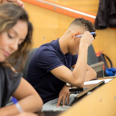 Tre studenter sitter i en hörsal i södra husen och skriver tentamen.