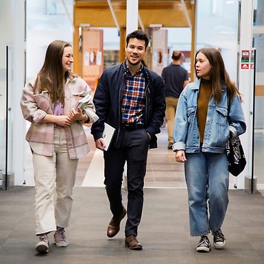 Tre personer går vid entrén till Stockholms universitetsbibliotek.