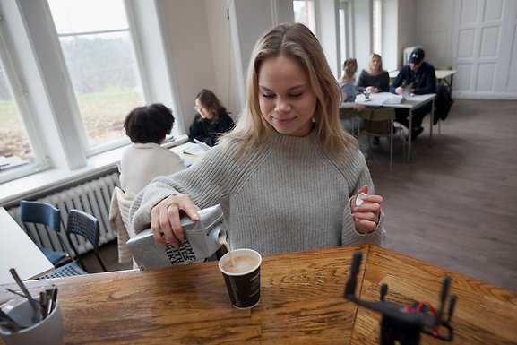 Student häller upp mjölk i kaffe.