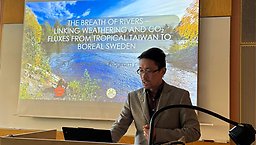 Researcher giving a presentation. Standing in front of a wide screen and looking down on a laptop