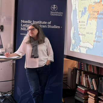 En person håller en presentation vid Nordiska Latinamerikainstitutet (Stockholms universitet) framför en projicerad historisk karta över Sverige och Finland. På kartan markeras områden kopplade till bland andra Kung Birger, Hertig Valdemar och Hertig Erik.