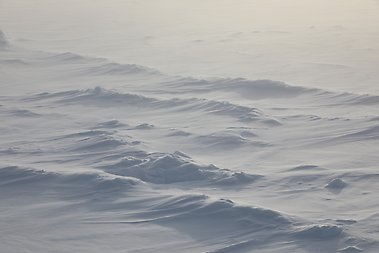 Snow accumulating around and blowing over sea ice ridges.