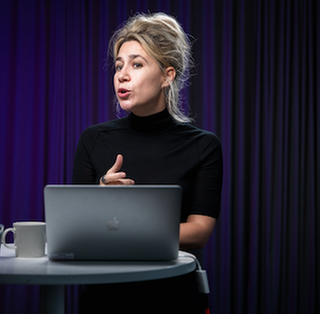 Photo of Sabina Čehajić-Clancy talking at a podium/stand table.