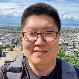 Wooseong Kim står på en höjd med en stad i bakgrunden. En solig dag.