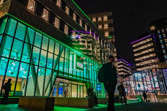 Personer med ryggsäckar utanför en upplyst kontorsbyggnad en sen kväll.
