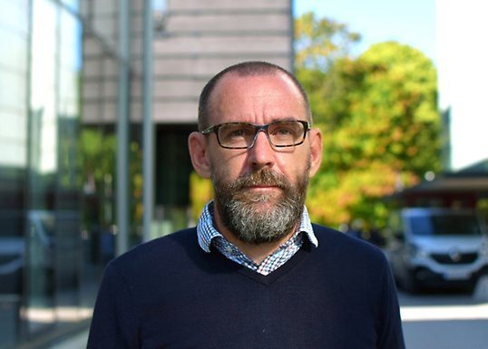 Michael Gähler står på campusområdet med grönska i bakgrunden.