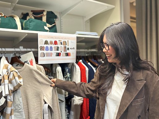 Person browsing clothing in a closet, holding a beige knit top on a hanger.