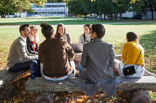 En grupp studenter sitter på bänkar utomhus