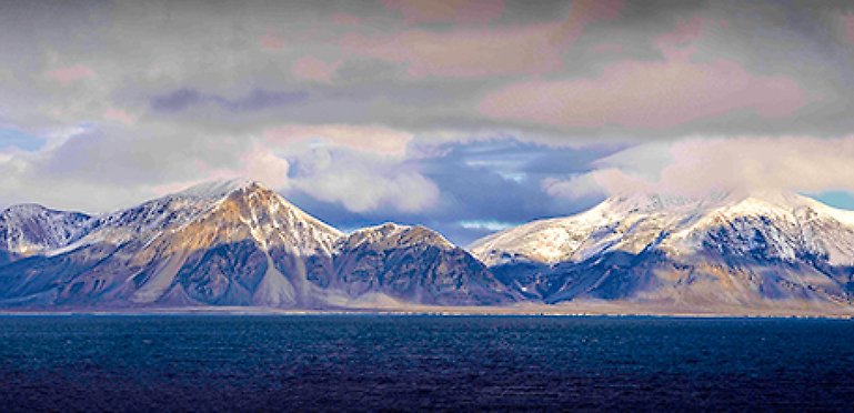 Mountains with snow tops, low clouds and the sun shining through.