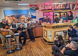 Three persons playing instruments, a bar and an audience.