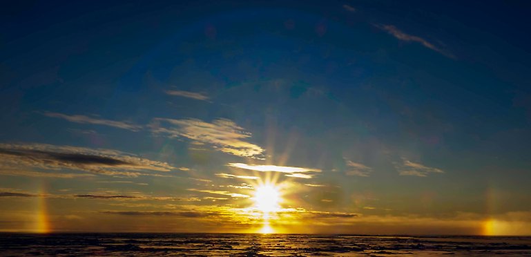 The sun, golden and darkblue sky and clouds, halo, sundogs, water.