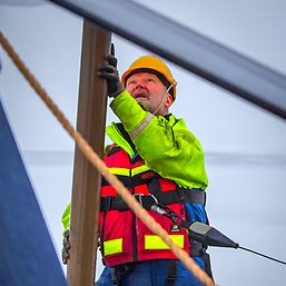 A man in lifewest, safety belt and helmet holding the sediment core.