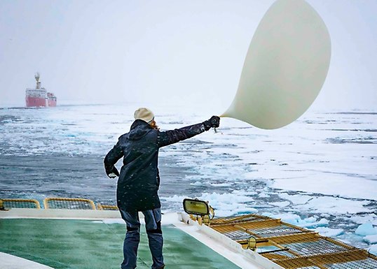 PhD student standing on deck struggling with big balloon bending in the wind.