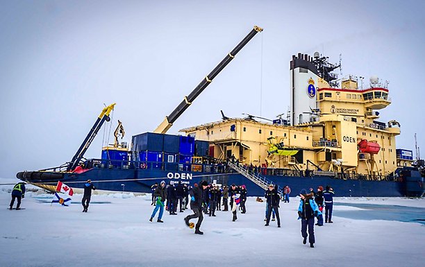 People playing on the ice, with icebreaker Oden in the vackground.