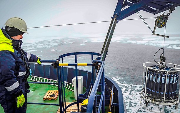 A researcher in helmet and outdoor clothes on icebreaker Oden looks at water sample "bottles".