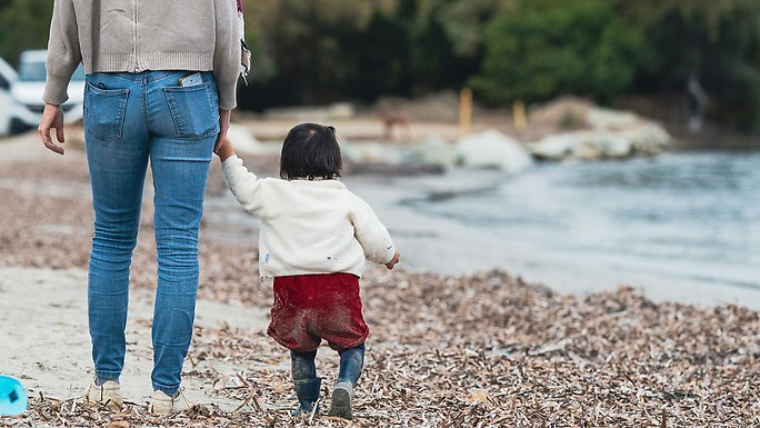 Kvinna går med sin lilla dotter längs en strand.