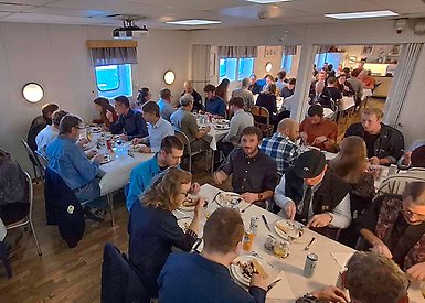 Många människor sitter och äter vid flera bord med vita linnedukar.