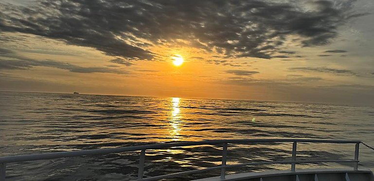 Solnedgång över havet. Mörka moln reflekteras i vattnet.