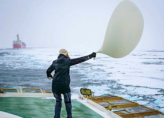 Doktorand står på däck och håller i stor ballong som rör sig i blåsten.