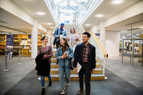 A group of students going down the stairs at the university library, talking and smiling.