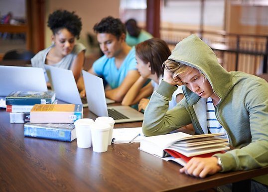 Studenter sitter vid ett bor och läser eller pratar med varandra.