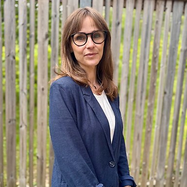 Sommarbild utomhus på Anna Ahlgren ståendes framför högt staket.