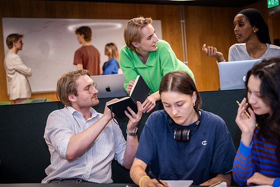 A group of students looking at an open book and discussing.