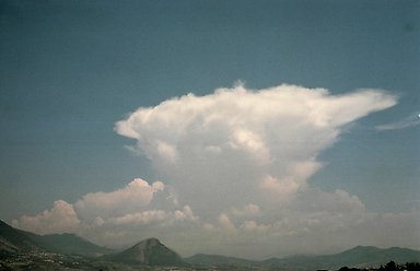 Gråblå himmel, berglandskap, högt vitt moln med formen av ett städ.