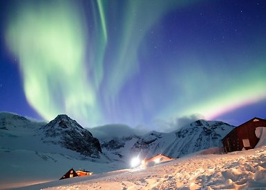Green and a bit pink Aurora Borealis, blue sky, mountains, snow and tents.