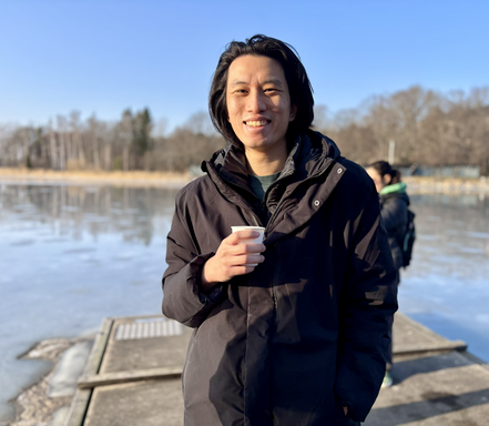 Student Chek Yia Choi holding a cup of hot coffee after a cold swim, warming up outdoors.