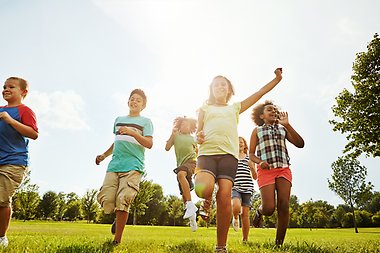 En grupp barn leker och springer i solen på ett gräsfält.