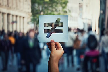 En hand som håller ett pappersark med en symbol för orättvisa mot en bakgrund av en folktät gata.