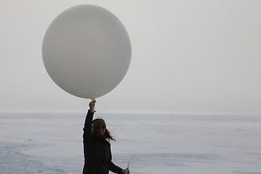 Woman holding a large gray-white balloon over her head, ready to release.