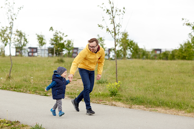 Pappa och liten son springer längs en gångväg i ett bostadsområde.