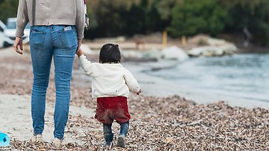 Kvinna går med sin lilla dotter längs en strand.