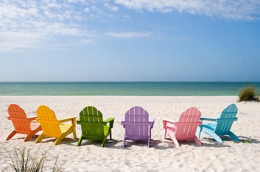 Sunchairs in different colours on a beach, facing the ocean.