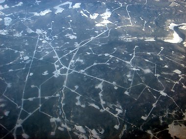 Flygfoto över ett oljefält i Alberta, Kanada, som visar ett nätverk av isiga vägar och borrningsplatser utspridda över ett snötäckt och skogklätt landskap.
