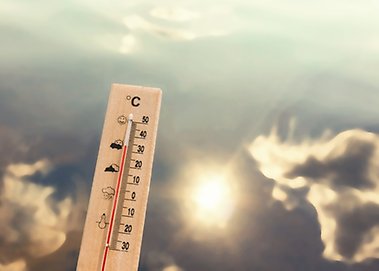 Termometer hålls upp mot himmel, sol och moln.