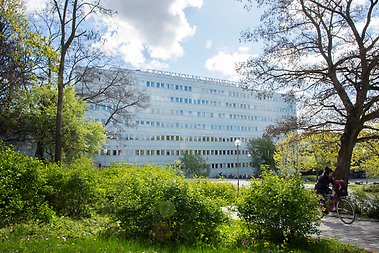 Campusbyggnad som det står Stockholms universtet på, omgiven av grönska.