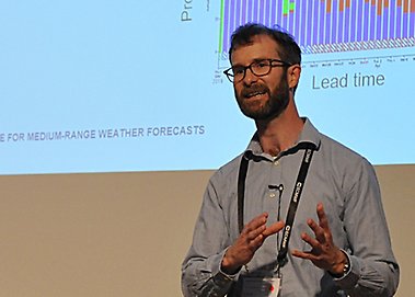 Linus standing talking and gesturing in front of a big screen presentation.