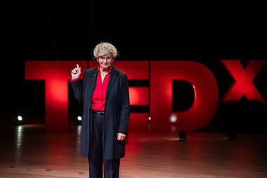 Kvinna håller upp fingret i luften. I bakgrunden står det TEDx. 