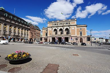 Exteriör av Kungliga Operan i Stockholm en solig dag, med svenska flaggan på taket.