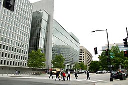 A group of people walking across a street next to tall buildings.