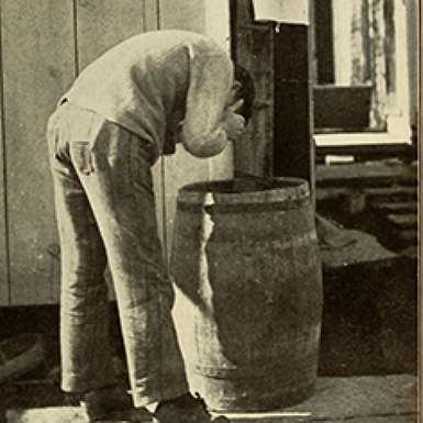 Picture of a man standing by a water barrel washing his face.