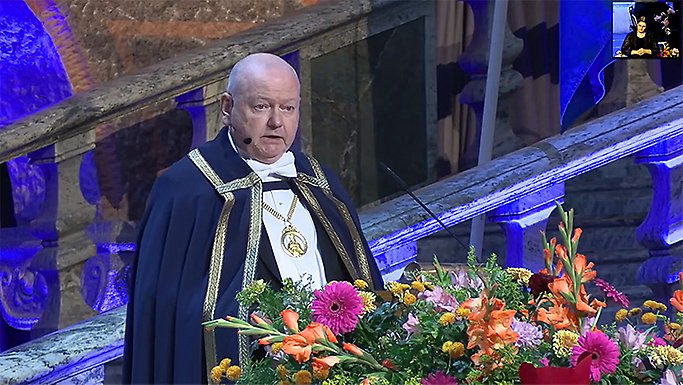 Hans Adolfsson i mantel, står vid podium smyckat med blommor.