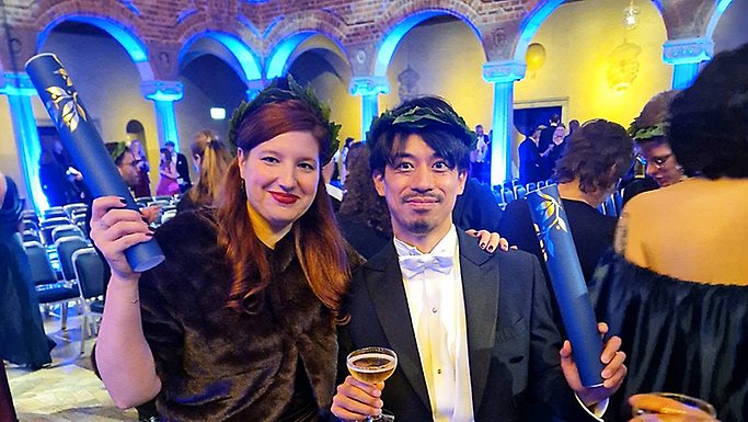 Milena Podolsak håller i diplomet och Shiro Shibata håller i diplomet och ett glas med dryck, i Blå hallen.