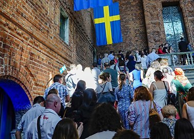 Många personer går uppför trappan i Stockholms Stadshus, en svensk flagga ovanför dem.