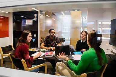 Fyra studenter sitter i ett grupprum och diskuterar.